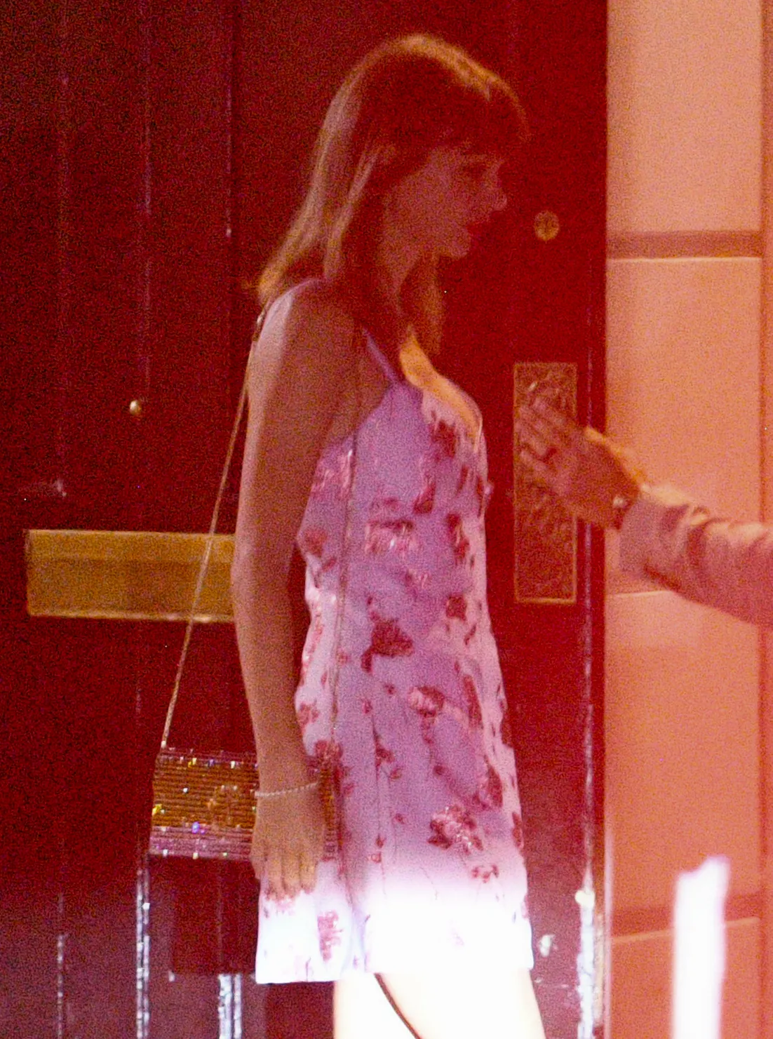 Taylor Swift in a pink and purple floral mini slip dress with a gold shoulder bag.
