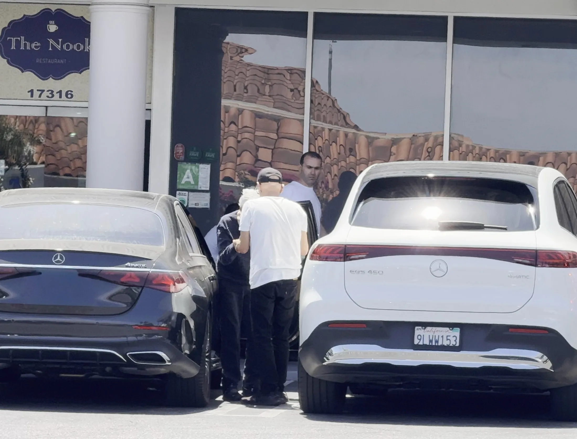 Frankie Valli in a wheelchair with a caretaker, exiting a black car in front of "The Nook Restaurant."