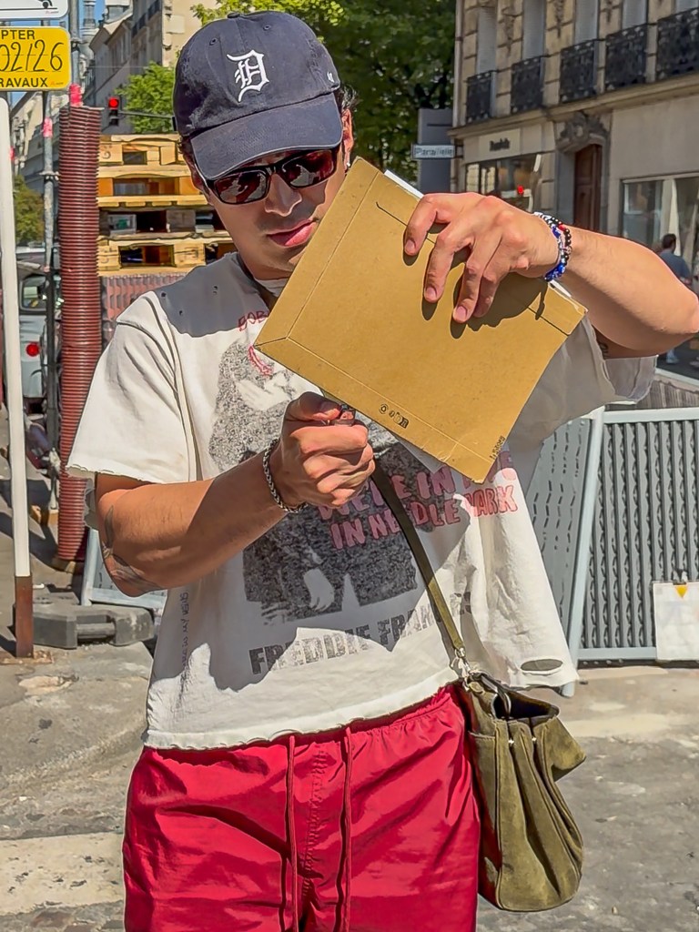 Hudson Williams holding a brown envelope and a lighter, appearing to threaten to burn the photos inside.