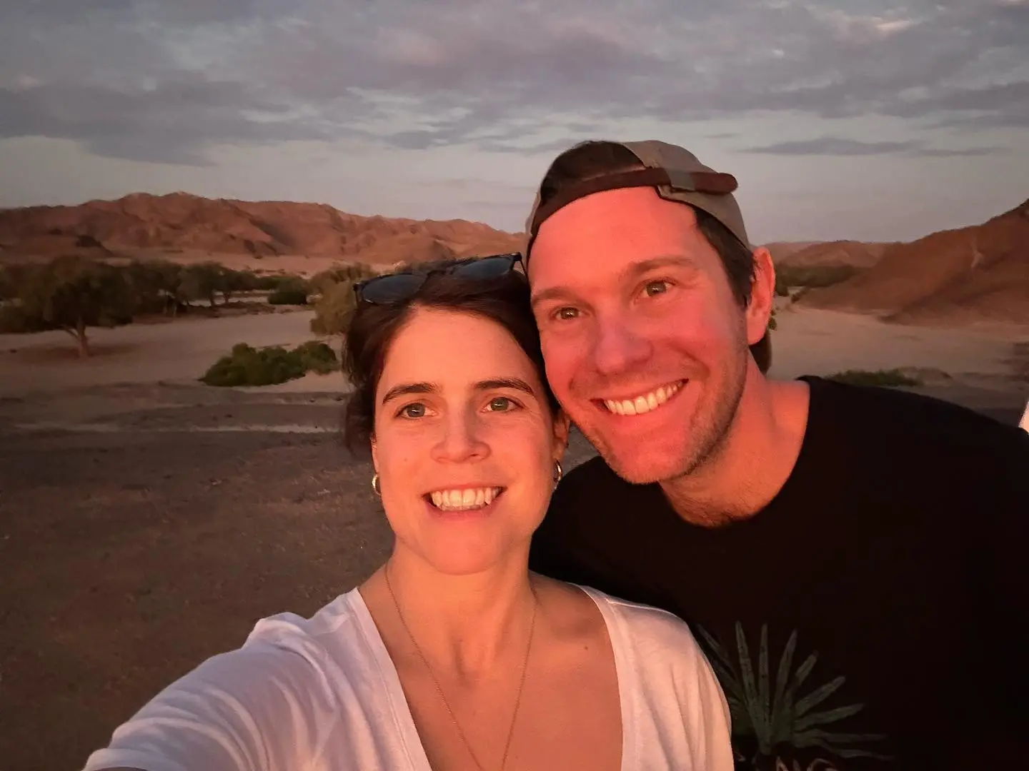 Princess Eugenie and Jack Brooksbank smiling together outdoors at sunset.