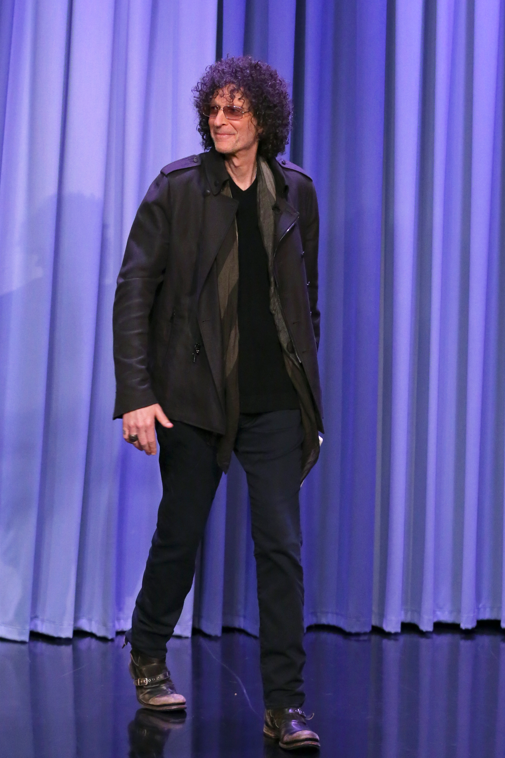 Howard Stern, a radio personality, walks towards the stage wearing sunglasses, a dark coat, and black pants.