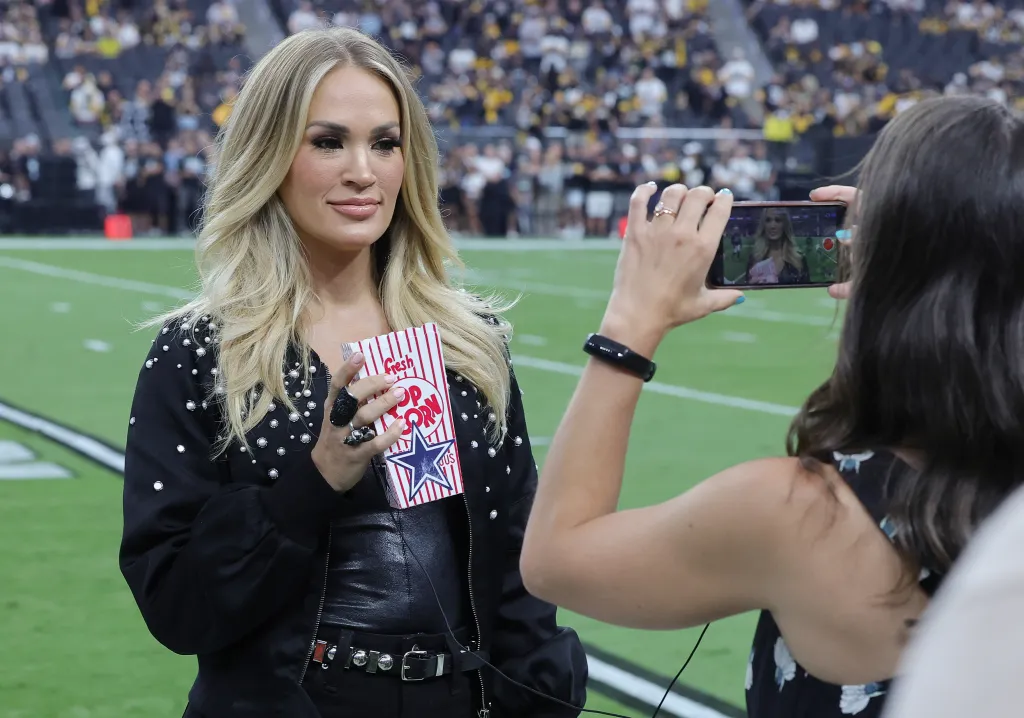 Recording artist Carrie Underwood films a promo on a football field, holding a "Fresh Popcorn" box with a Dallas Cowboys star.