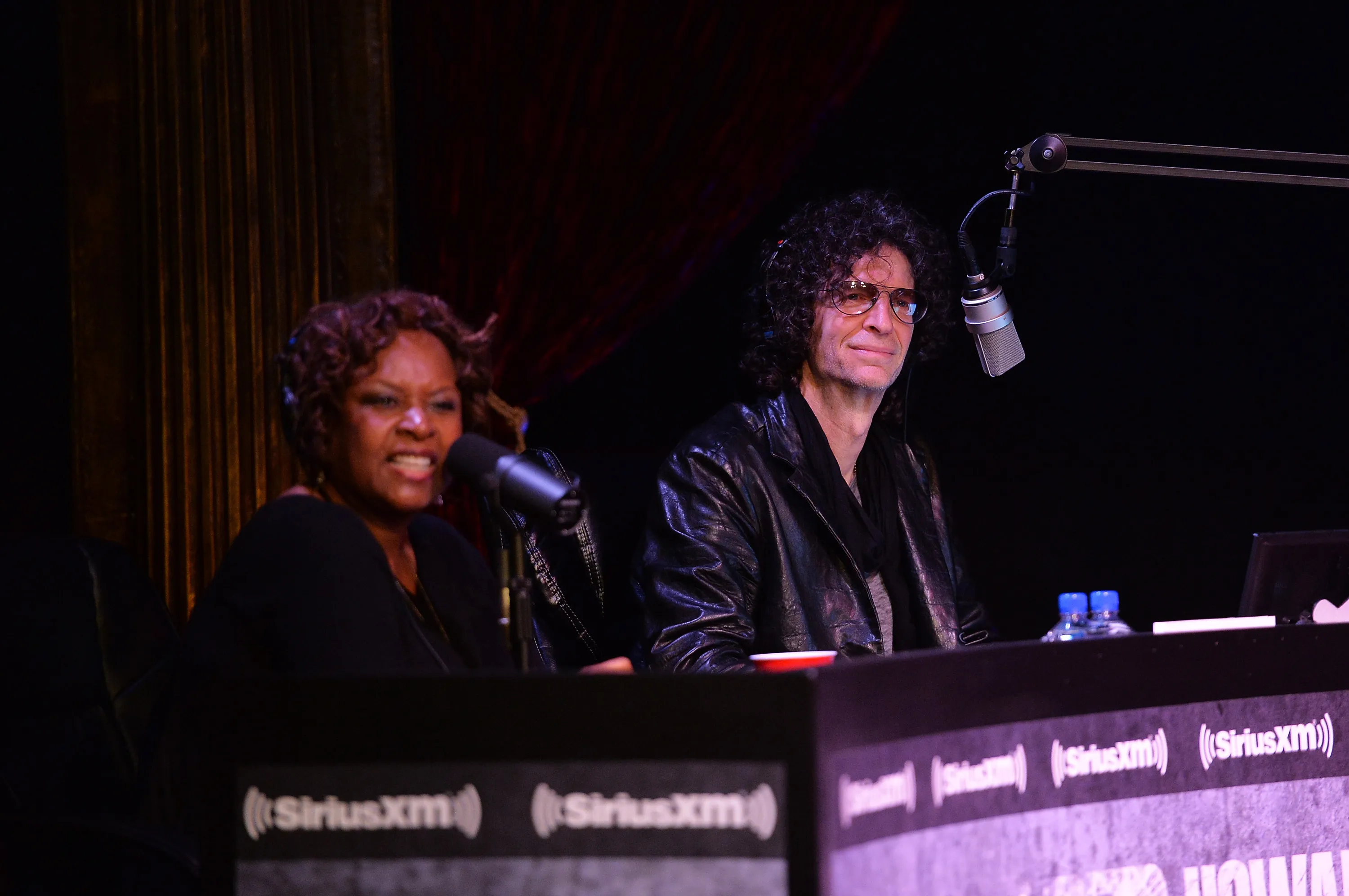 Robin Quivers and Howard Stern speaking into microphones at a SiriusXM Town Hall event.