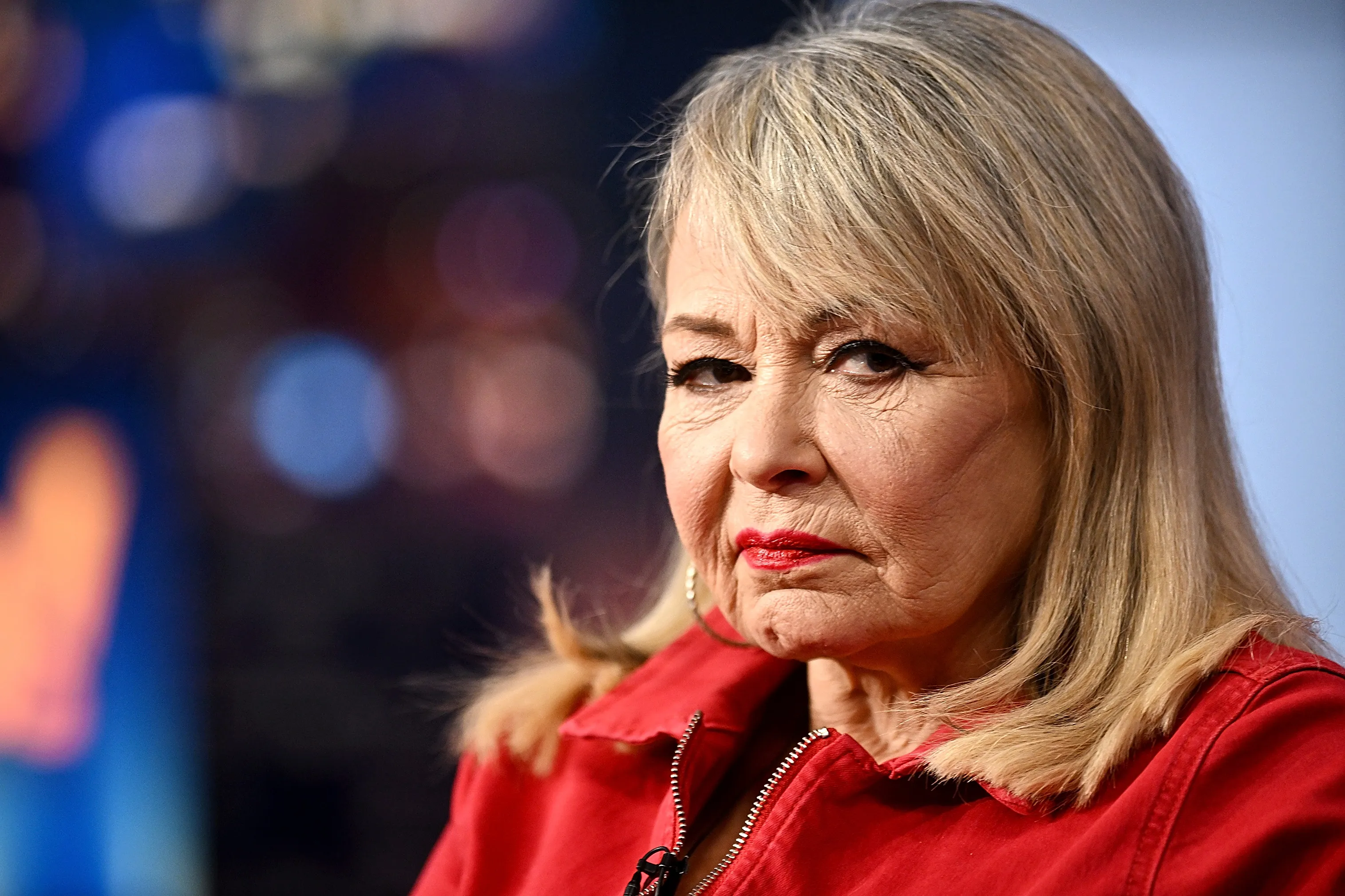 Roseanne Barr, host of FOX Nation’s “Cancel This!,” wearing a red jacket and red lipstick, looking towards the right.