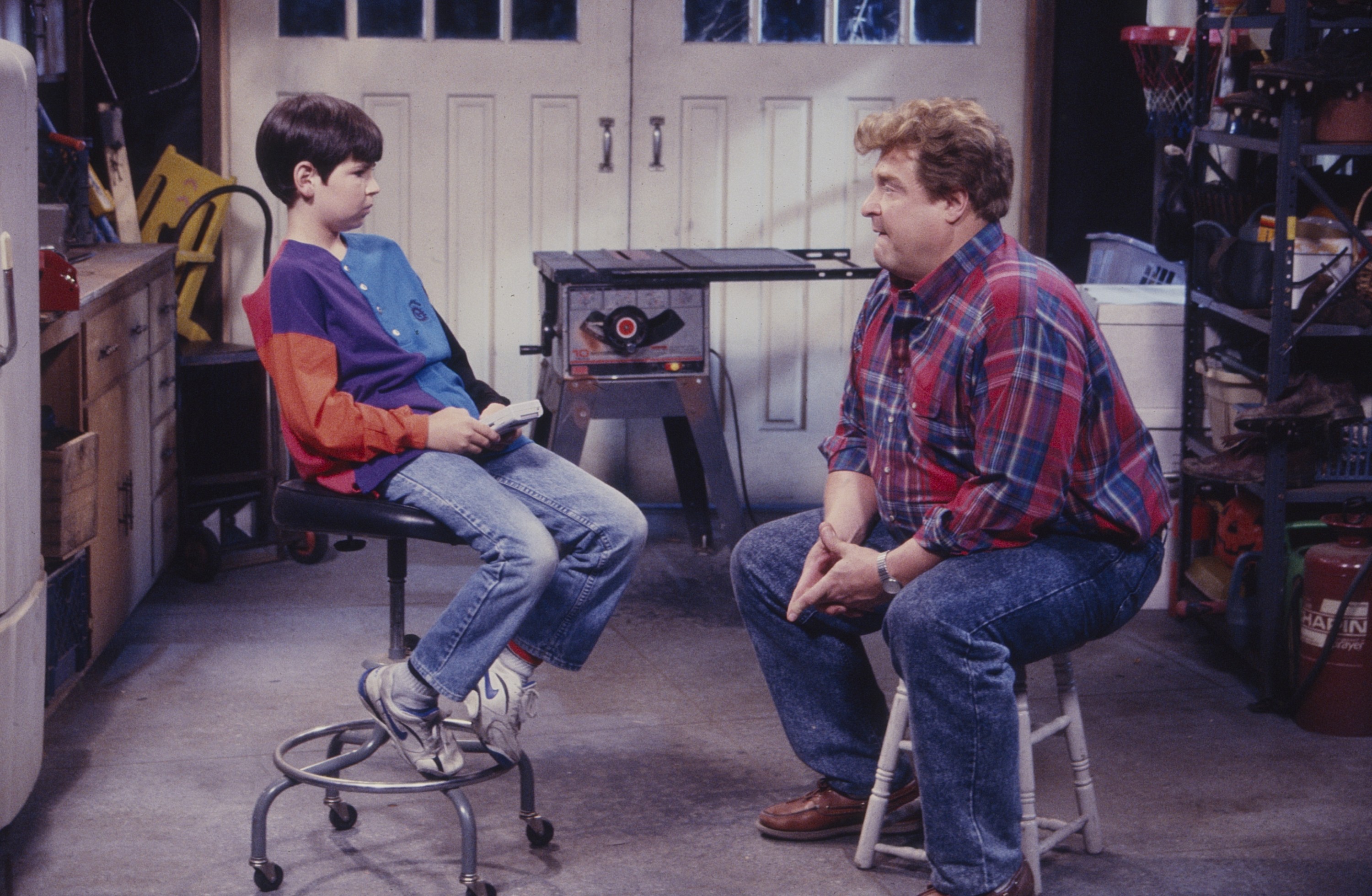 John Goodman and Michael Fishman seated in a garage, from "Roseanne".