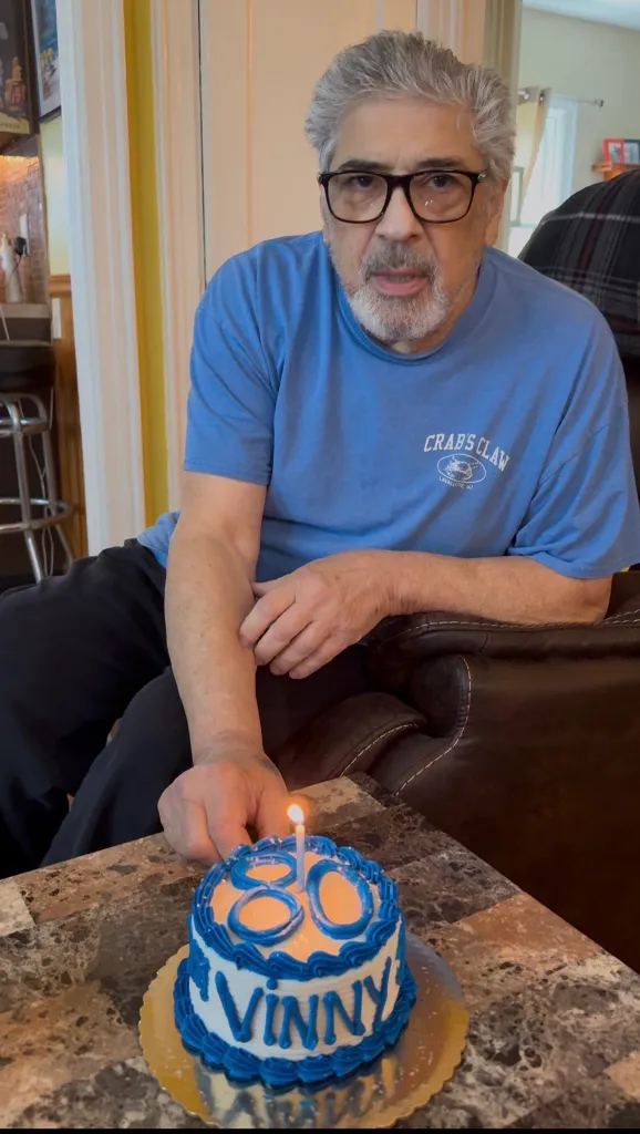 Man celebrating his 80th birthday with a cake that reads "Vinny".