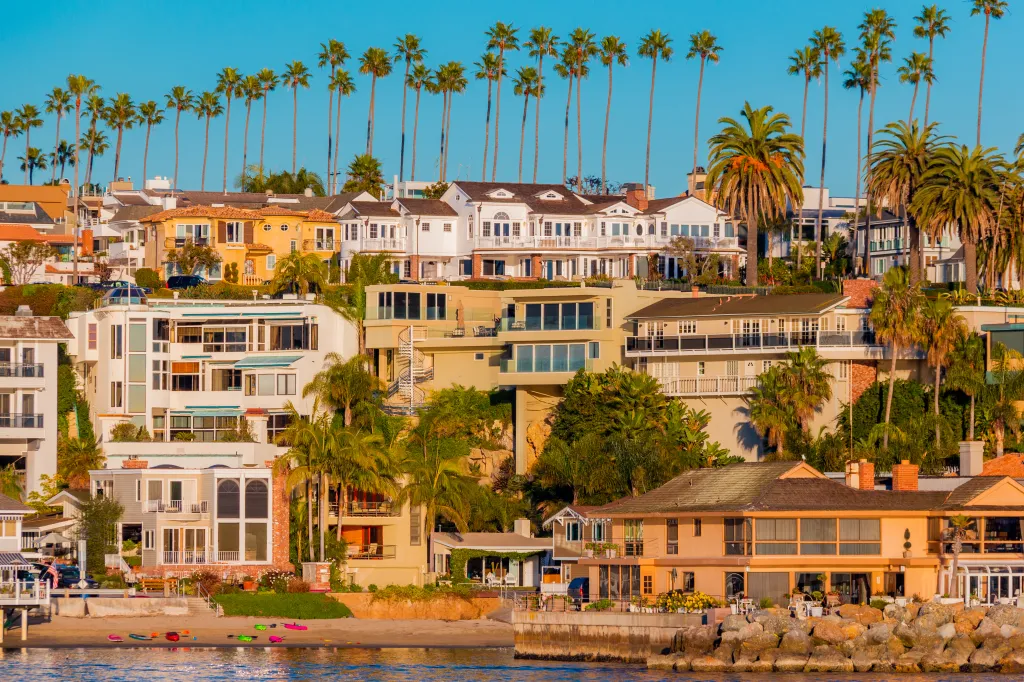 Multi-colored luxury beach houses lining the sidewalk next to their private beach and dock at Balboa Peninsula in Newport Beach, California.