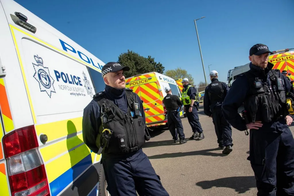 Two police officers standing by a police van, with more officers and vehicles in the background.