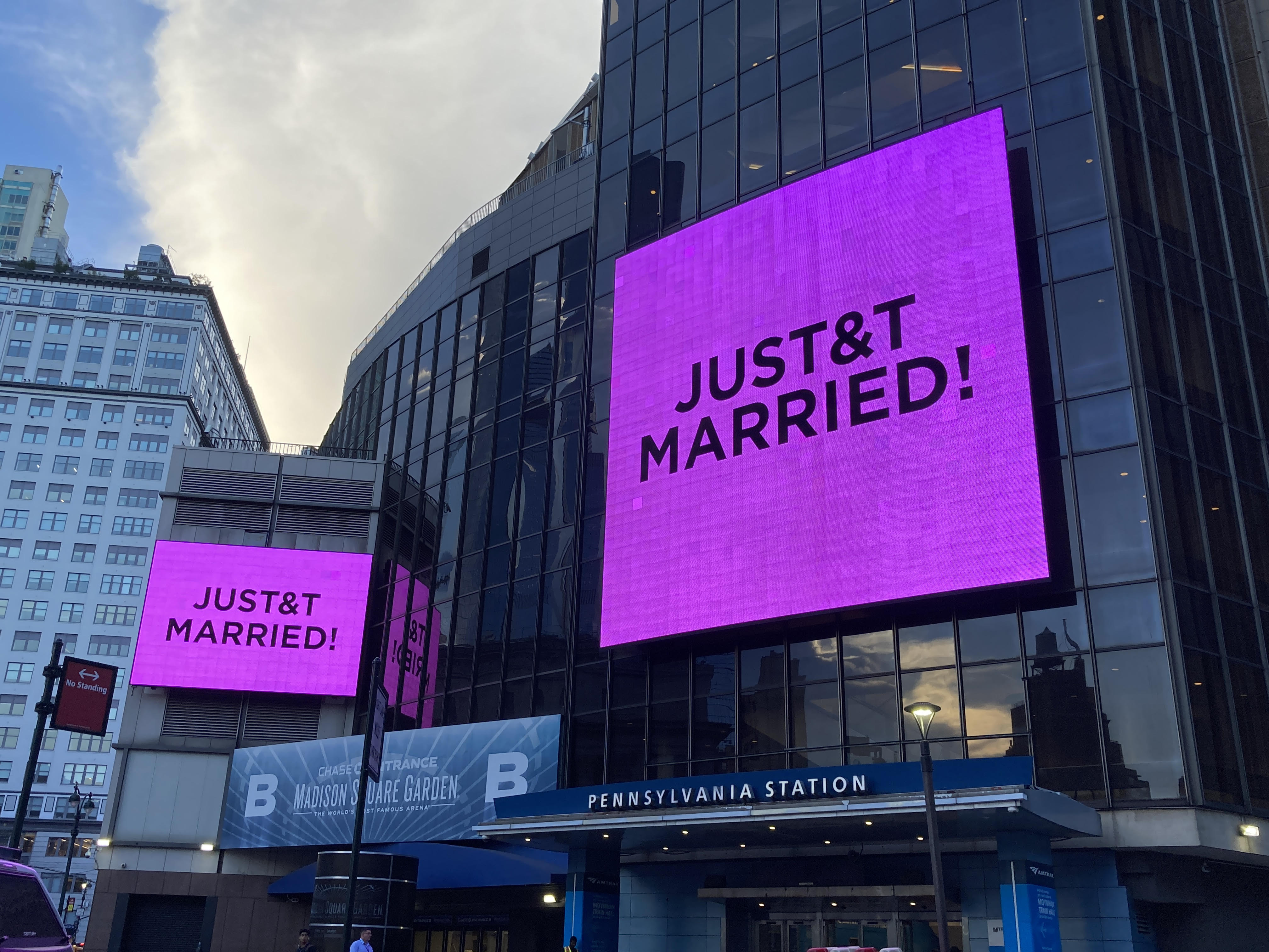 Two large purple screens outside Madison Square Garden and Pennsylvania Station display "JUST & T MARRIED!".