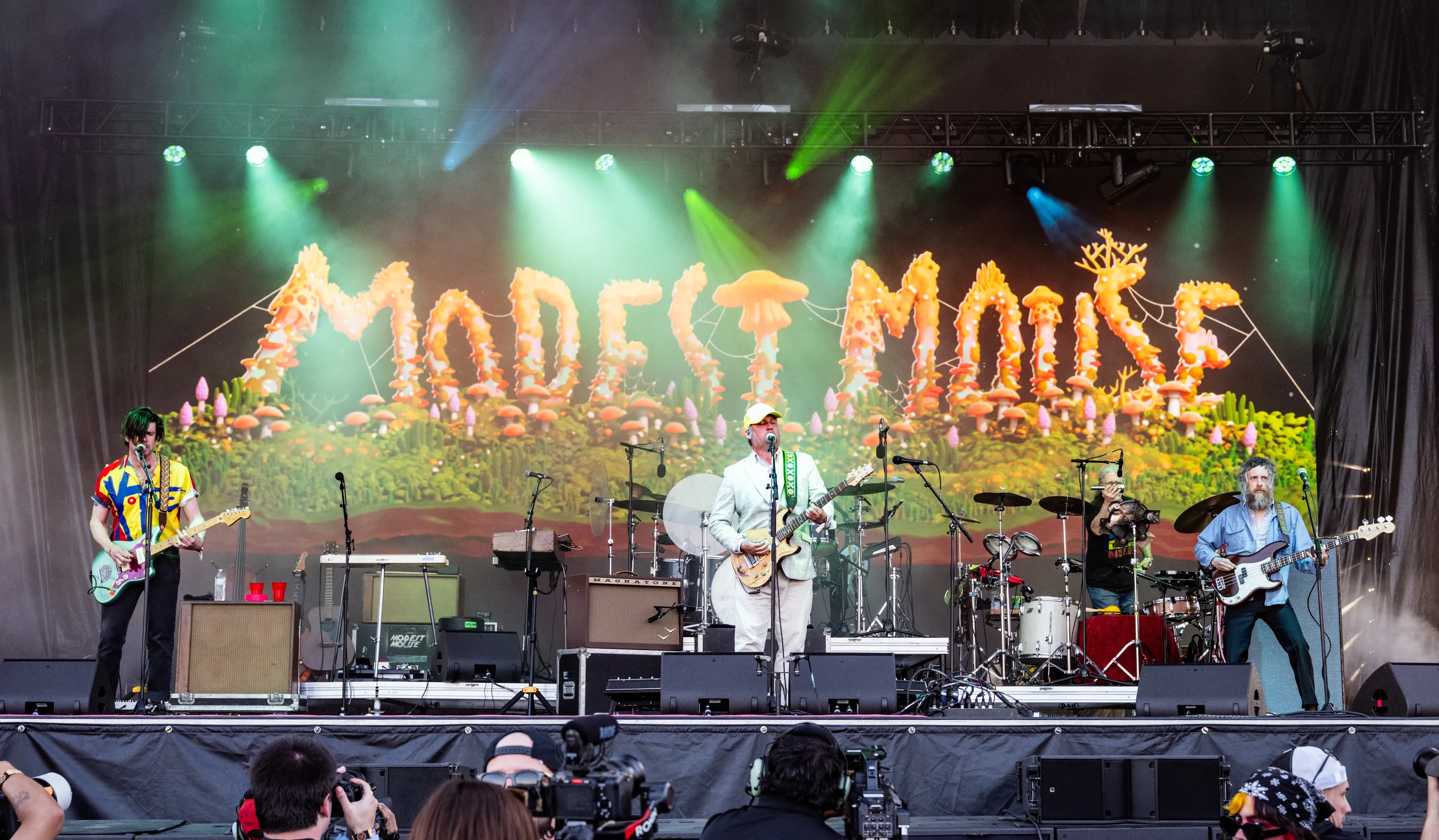 Modest Mouse performing on stage at Kilby Block Party, with the band's name stylized as mushrooms and other fungal decorations in the background.