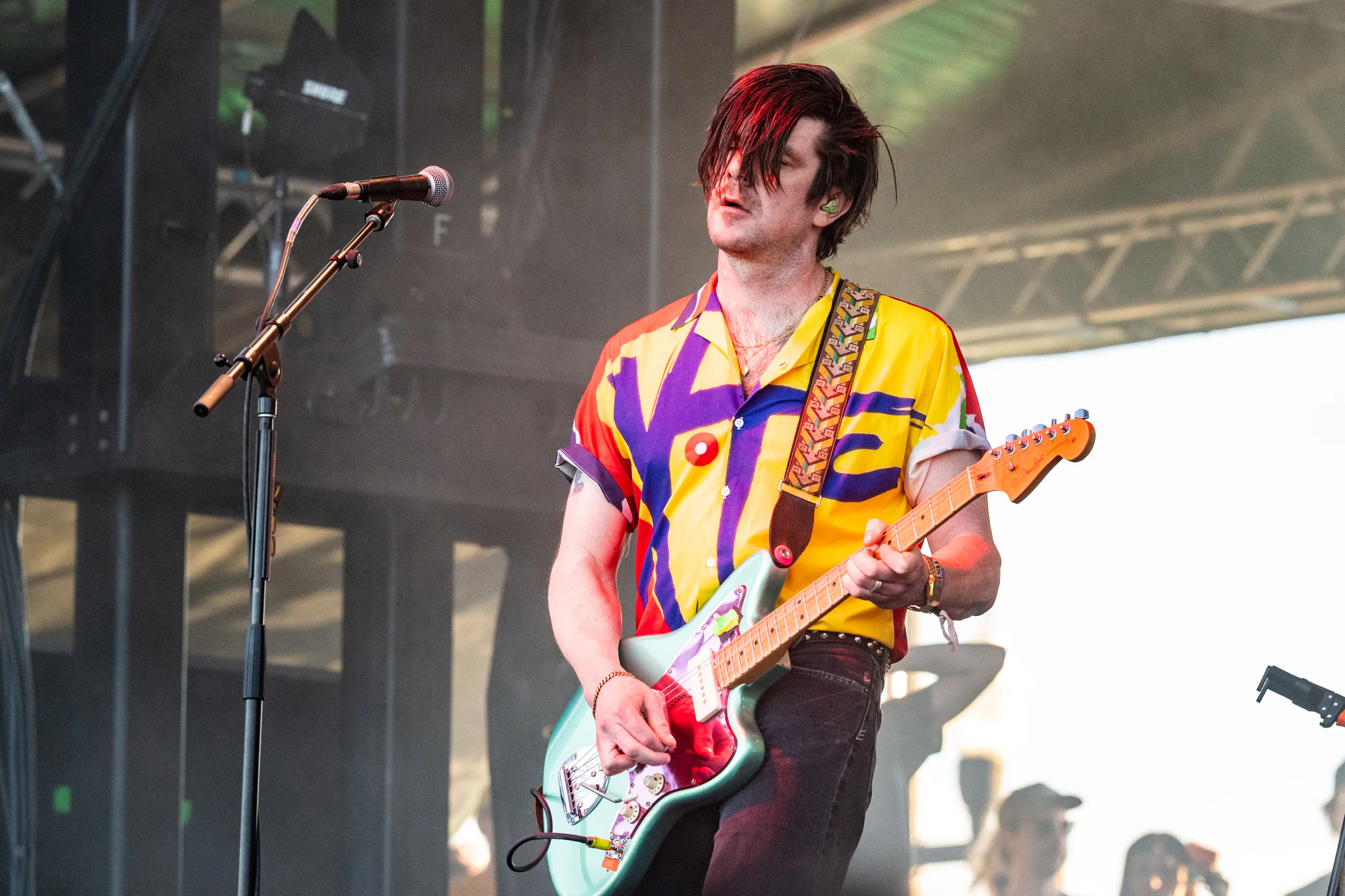 Simon O'Connor of Modest Mouse performs on stage, playing a light blue electric guitar.