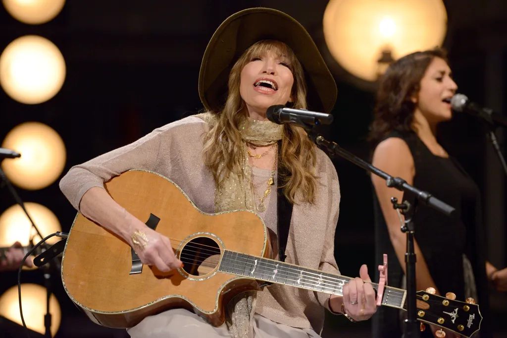 Carly Simon performing with her son Ben Taylor, while playing guitar and singing into a microphone.