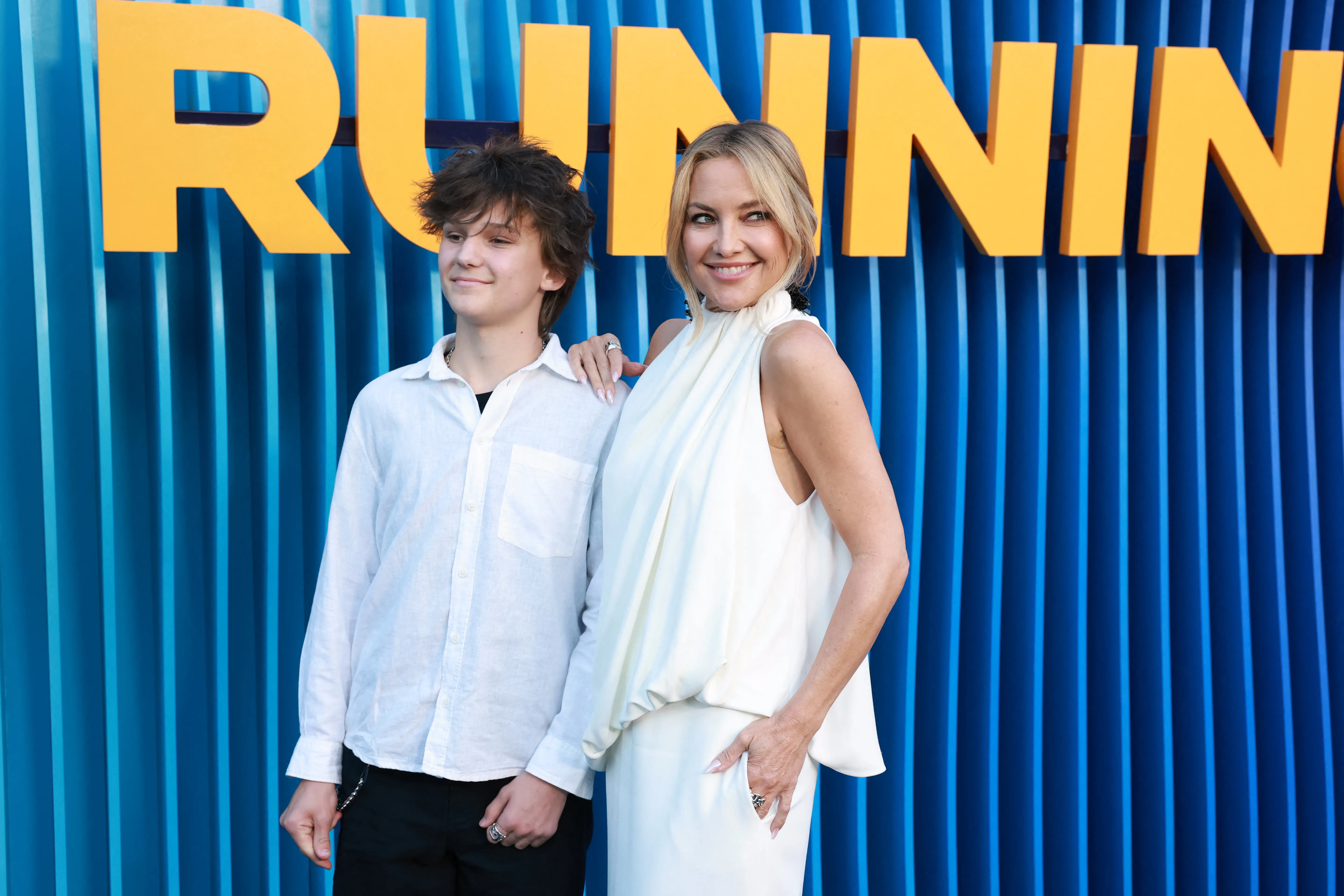 Actress Kate Hudson and her son Bingham Hawn Bellamy stand in front of a blue background with orange "RUNNING" text.