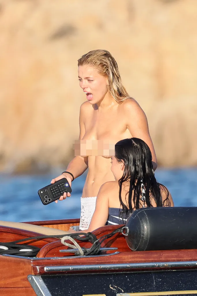 Brooks Nader holds a remote while topless in a boat with her sister Sarah Jane.