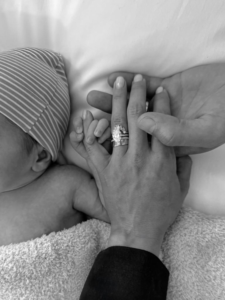 Stephen Colletti and Alex Weaver holding their newborn Rhodes August Colletti's hand.