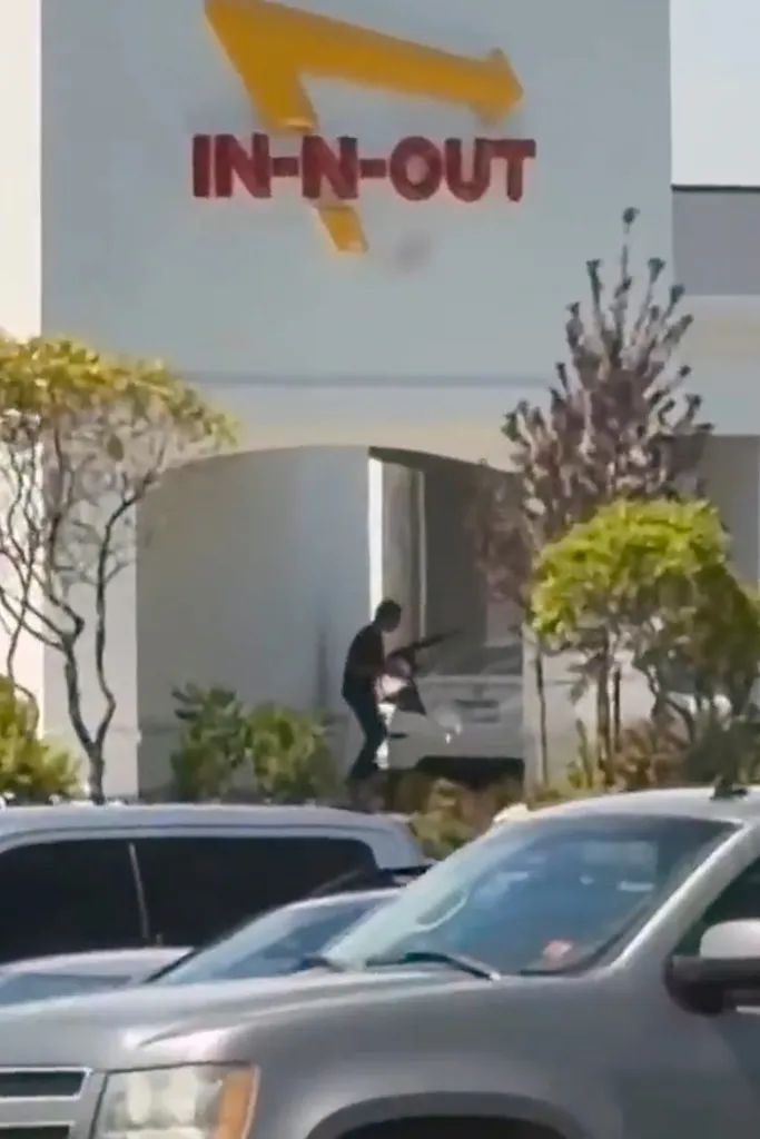 A person holding a rifle outside an In-N-Out Burger restaurant.