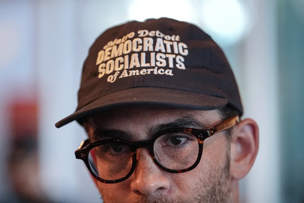 Streamer Hasan Piker wearing a "Metro Detroit Democratic Socialists of America" hat and glasses while canvassing in Detroit.