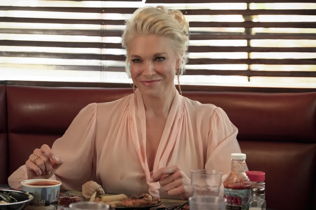 Rebecca Welton from Ted Lasso sits at a diner booth, smiling, with food and condiments on the table in front of her.