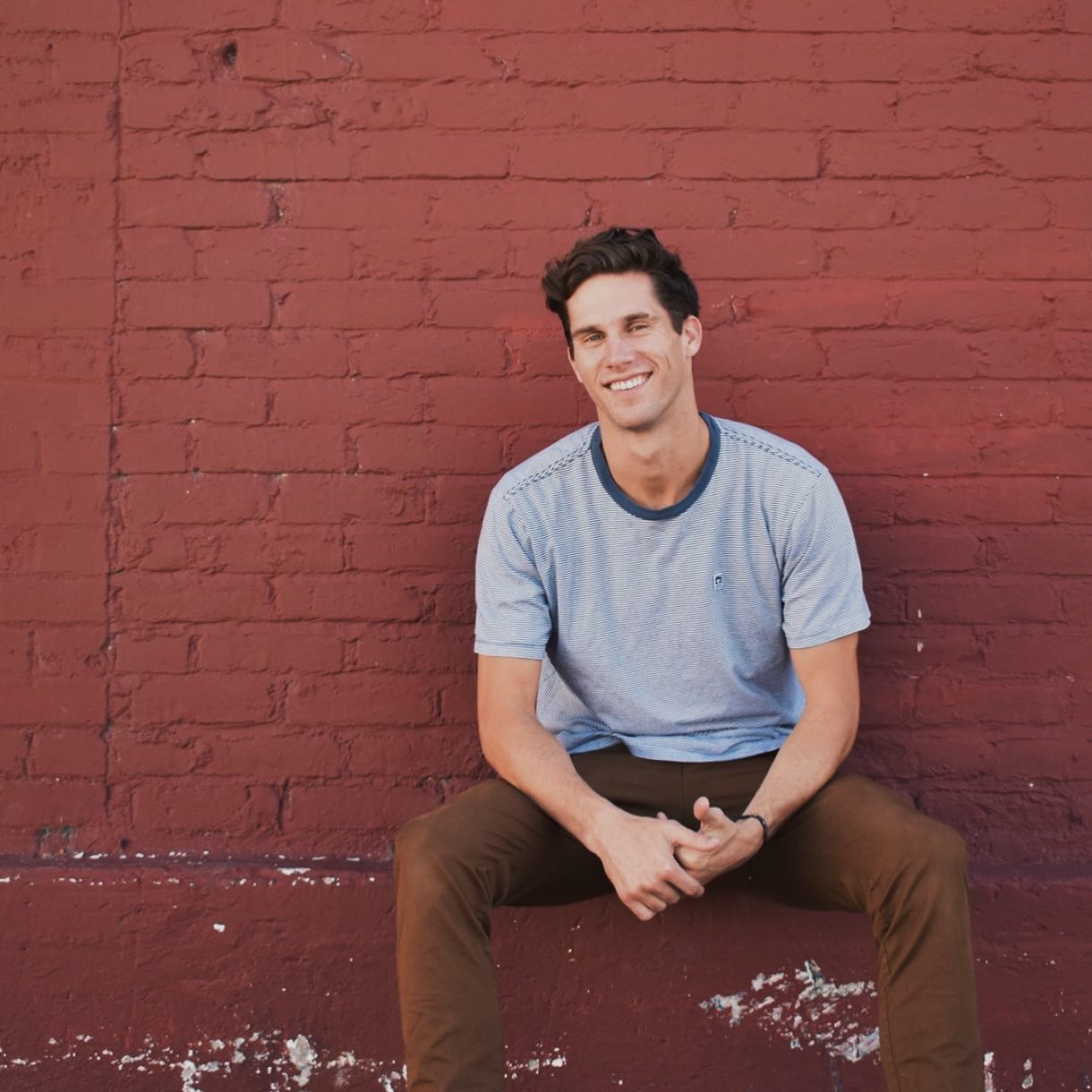 PJ Conley smiling and sitting against a brick wall.