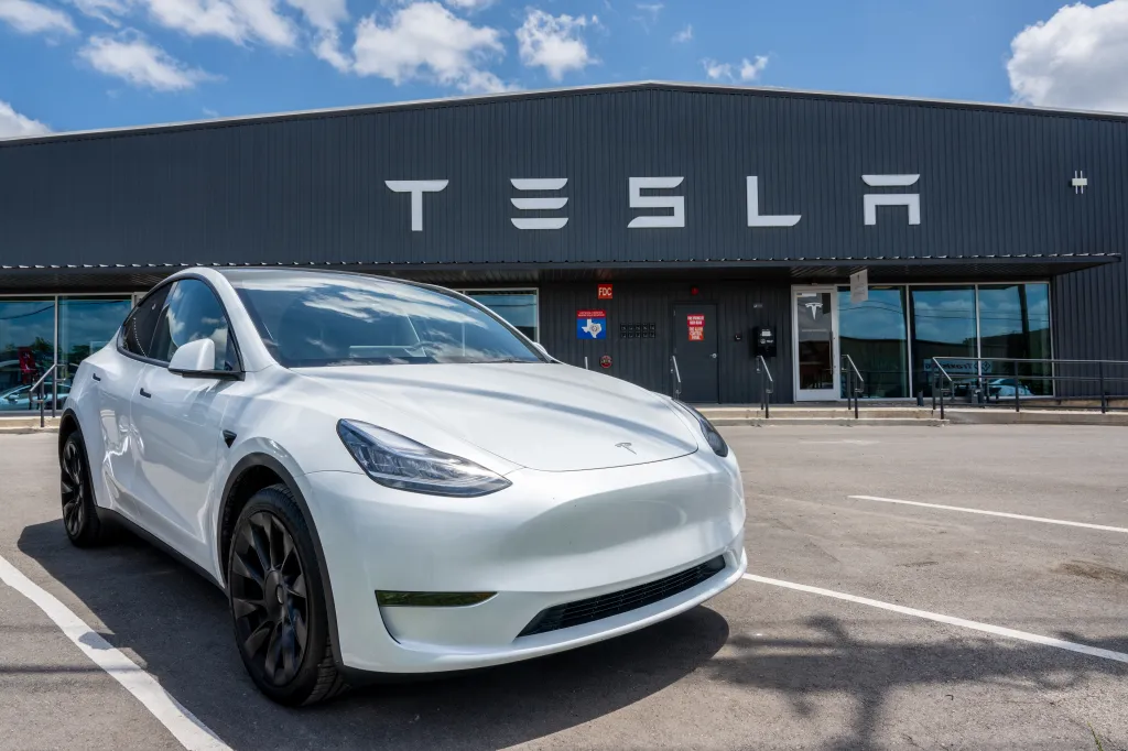 A white Tesla Model Y parked in front of a Tesla car lot.