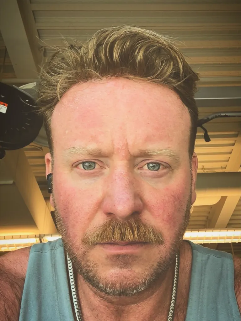 Tyler Duckworth, looking at the camera, sweaty, and wearing a blue tank top