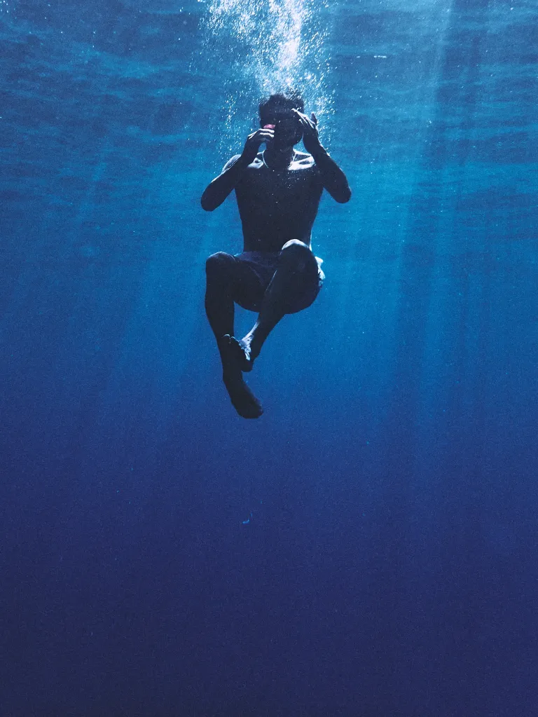 Tom Brady underwater in a blue ocean, looking up with bubbles above his head.