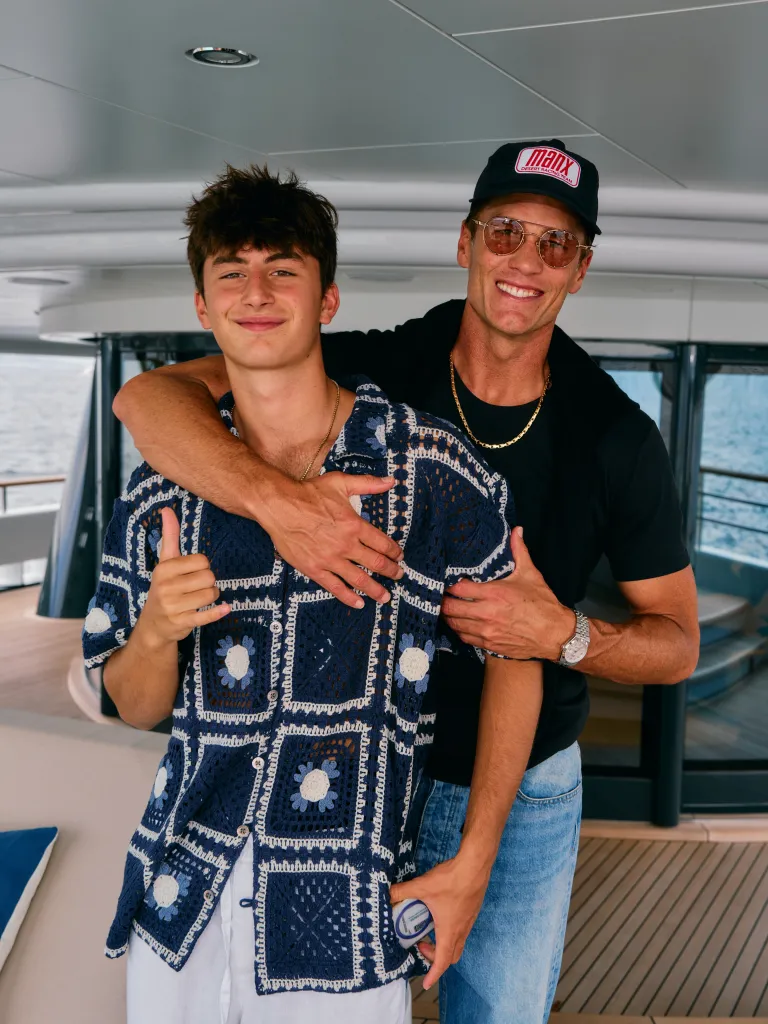 Tom Brady with his arm around his son, both smiling, on a boat.