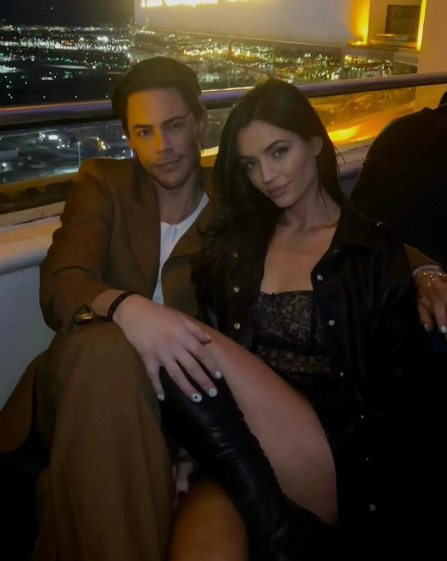 Tom Sandoval and Victoria Robinson posing together at night with city lights in the background.