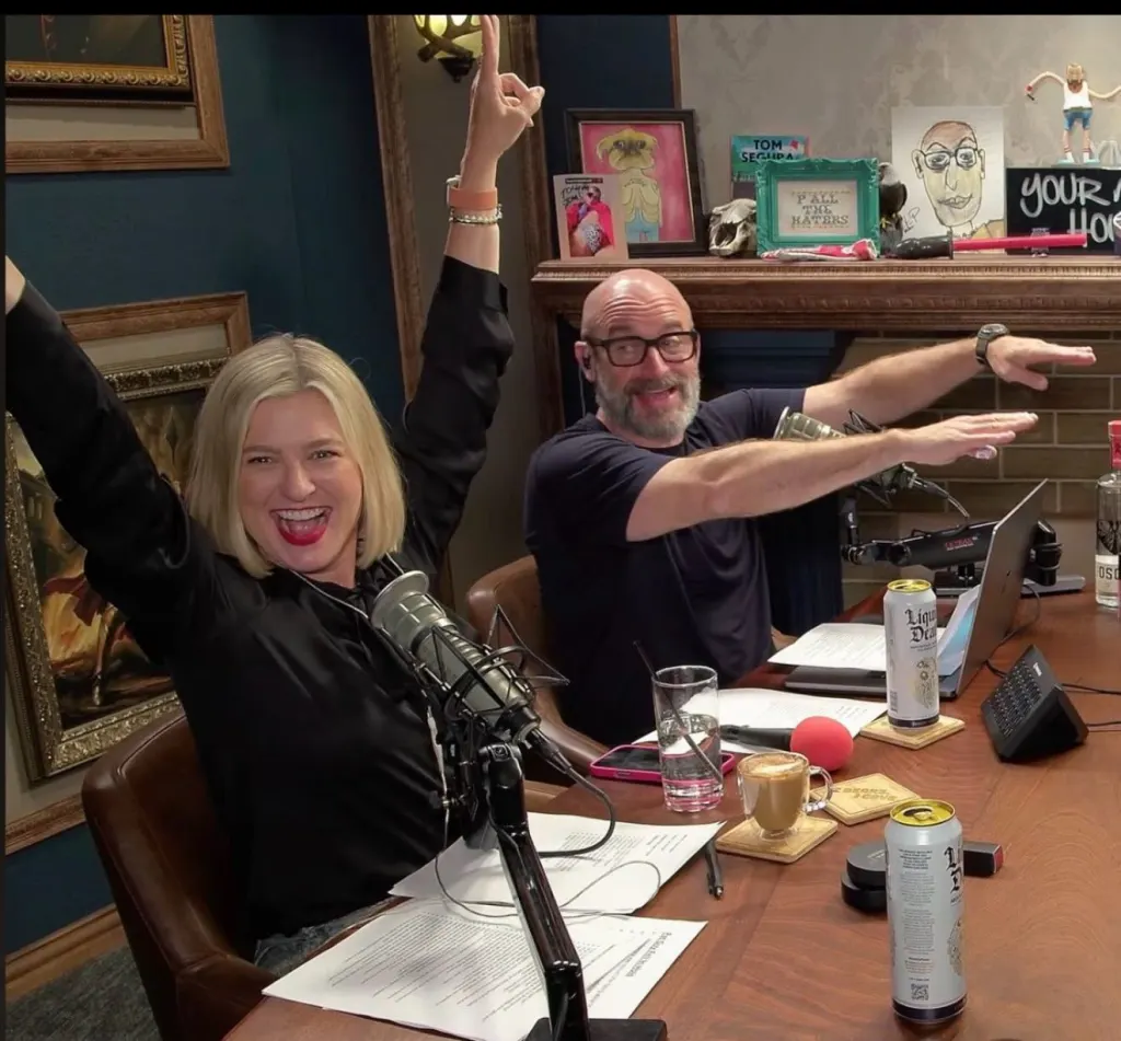 Christina Pazsitzky raising her arms and Tom Segura gesturing with his arms.