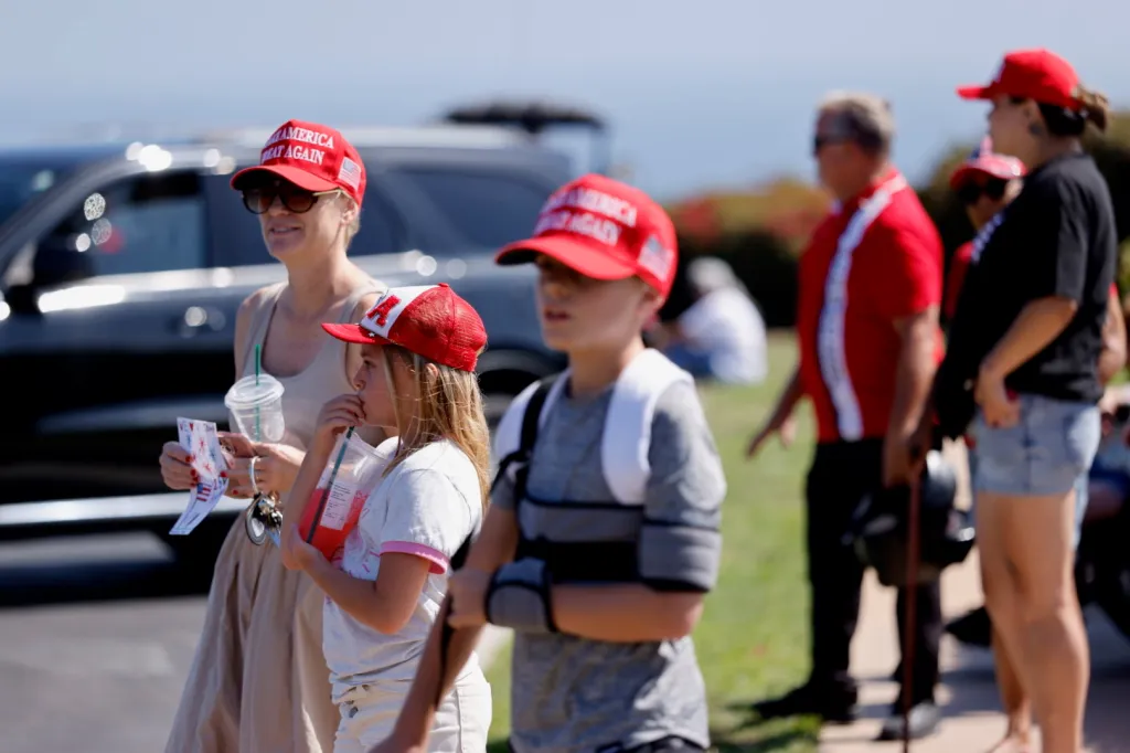 Trump supporters, including a woman and two children in red hats, gather outside the Trump National Golf Club.