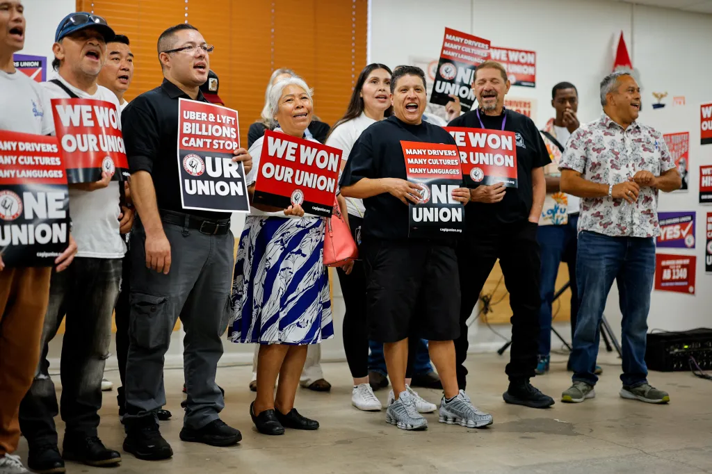 Uber and Lyft drivers celebrating at a press conference, holding signs to announce the formation of the California Gig Workers Union.