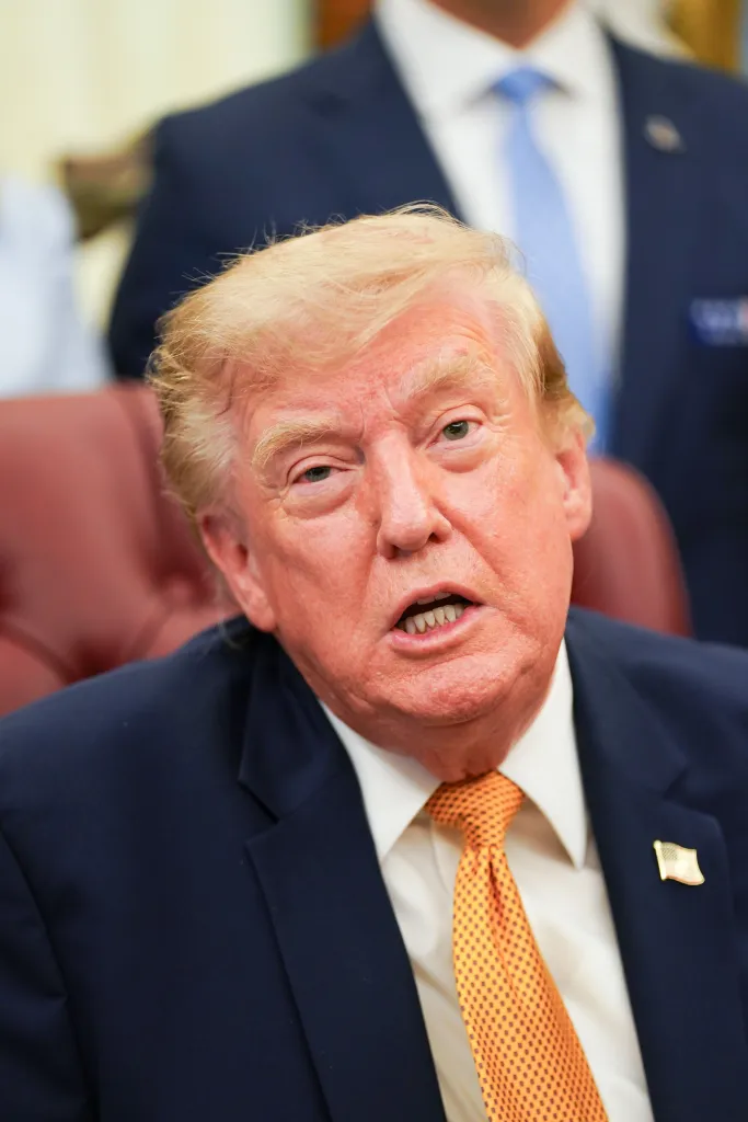 Donald Trump in a suit and orange tie speaking in the Oval Office.