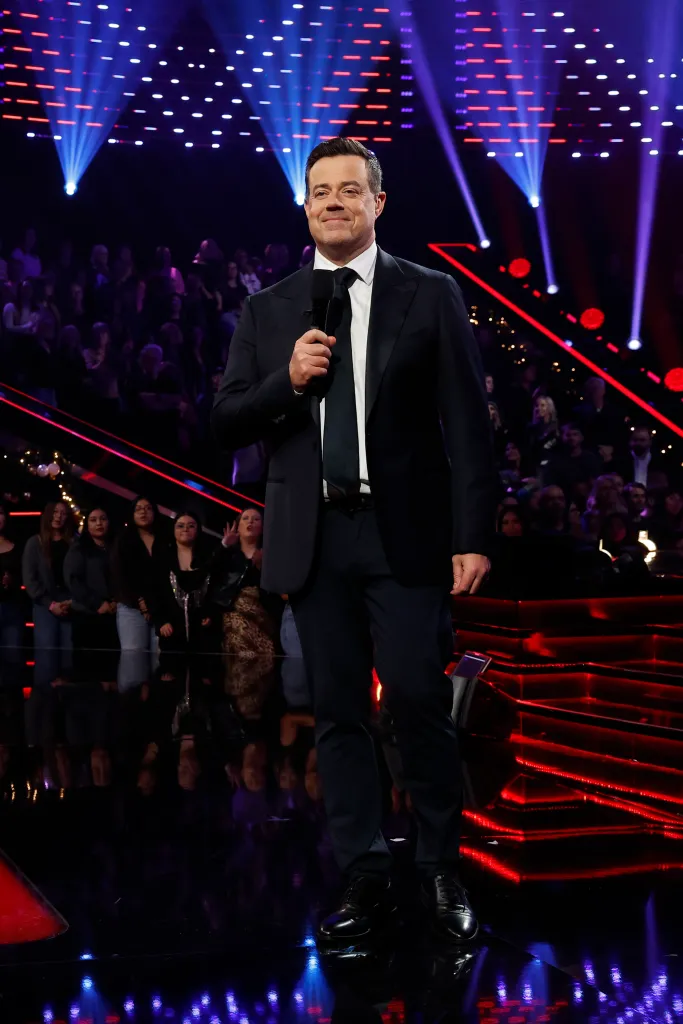 Carson Daly holding a microphone on "The Voice Live Finale Top 6 Performances" stage.