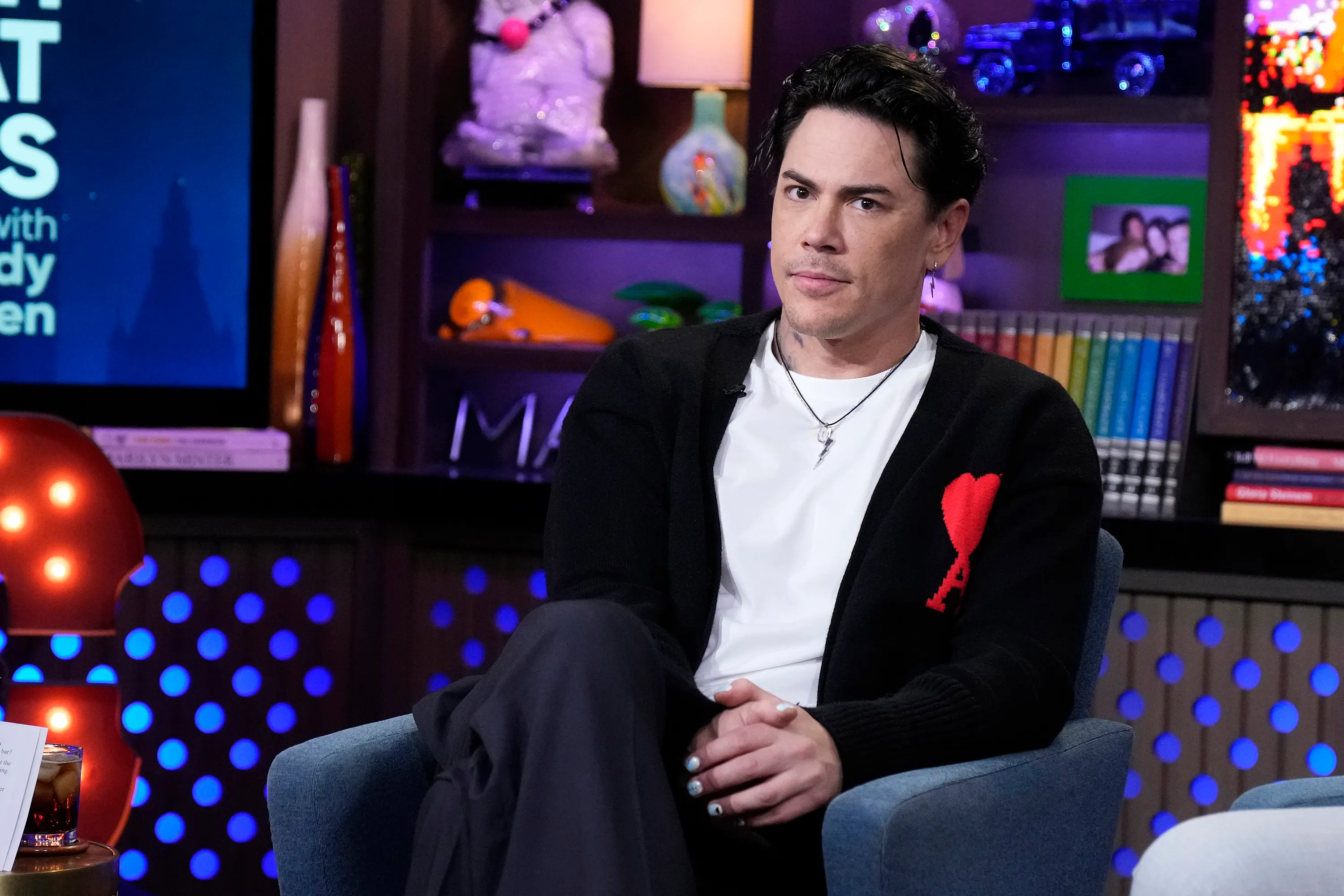 Tom Sandoval sitting in a blue chair wearing a black cardigan over a white shirt.