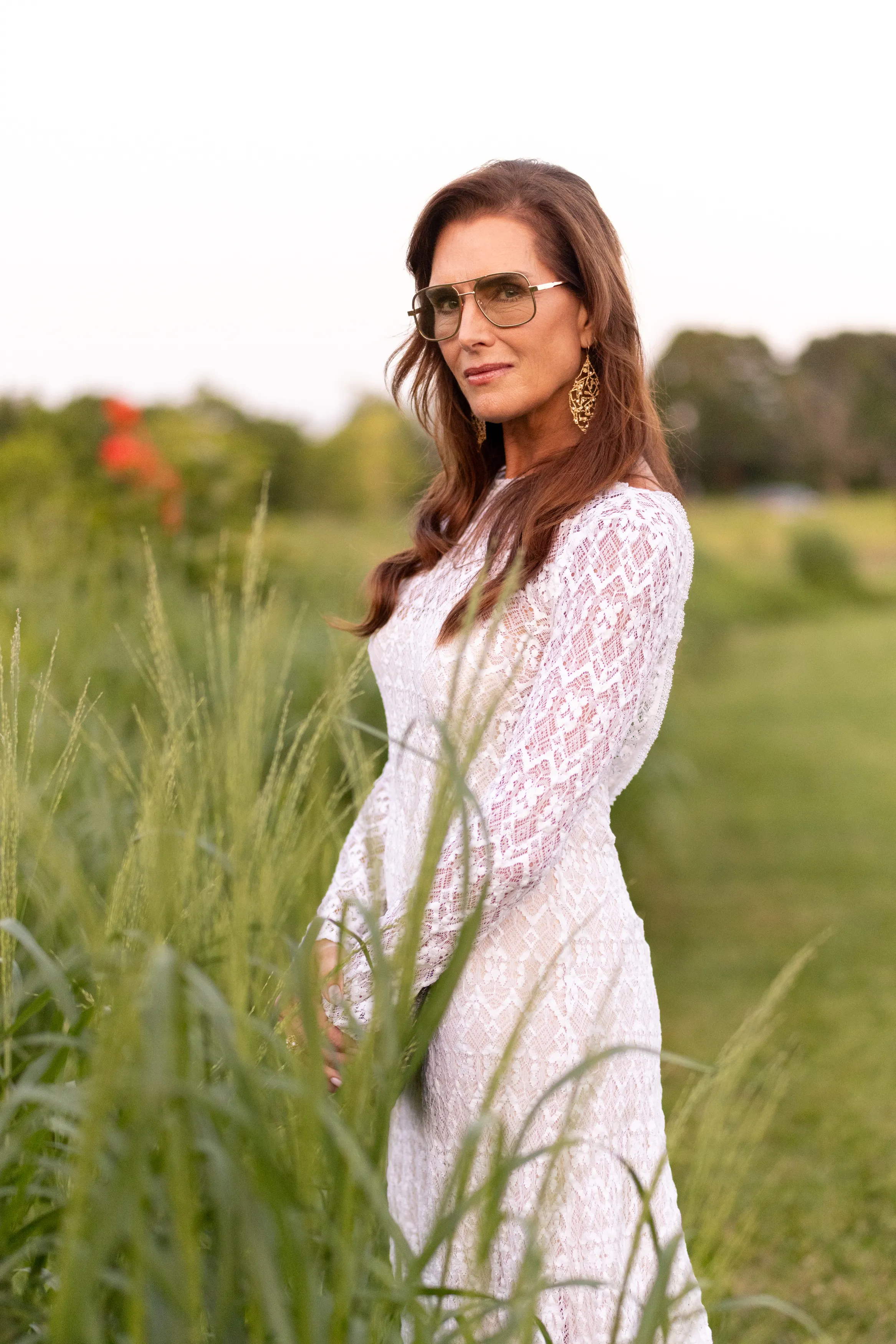 Brooke Shields poses outdoors in a white lace dress and sunglasses.