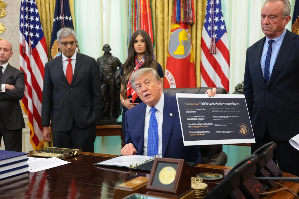 Trump, accompanied by (L-R) White House Deputy Chief of Staff and Homeland Security Advisor Stephen Miller, National Institutes of Health Director Jay Bhattacharya, Jayme Leagh Franklin with the The Conservateur, and Health and Human Services Secretary Robert F. Kennedy Jr., holds up a sign that reads "Gold Standard Childhood Vaccine Recommendations" before signing an executive order calling for childhood vaccine shots to be spaced out into separate visits during an event in the Oval Office of the White House on August 10, 2026