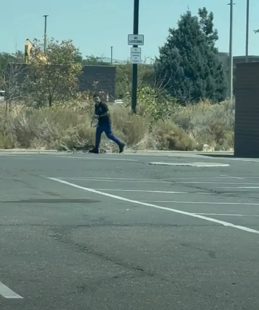 A man running across a parking lot while carrying a rifle.