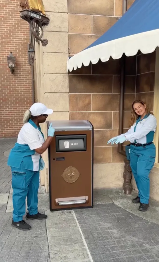 Two women in blue and white uniforms demonstrating a trash can at Disney.