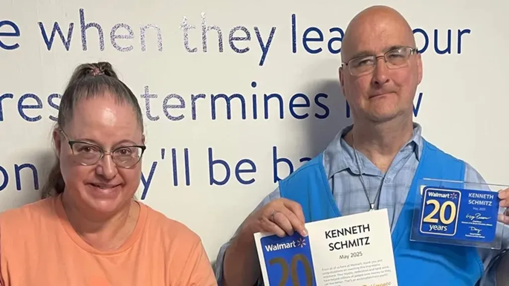 A man wearing a blue Walmart vest holds a certificate and plaque for 20 years of service, standing next to a smiling woman.