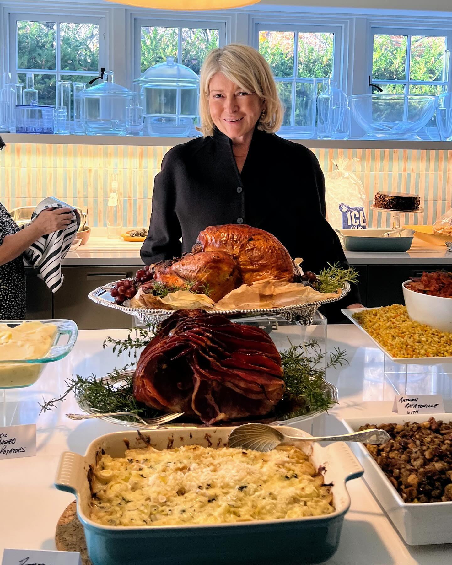Martha Stewart standing behind a large spread of Thanksgiving food.