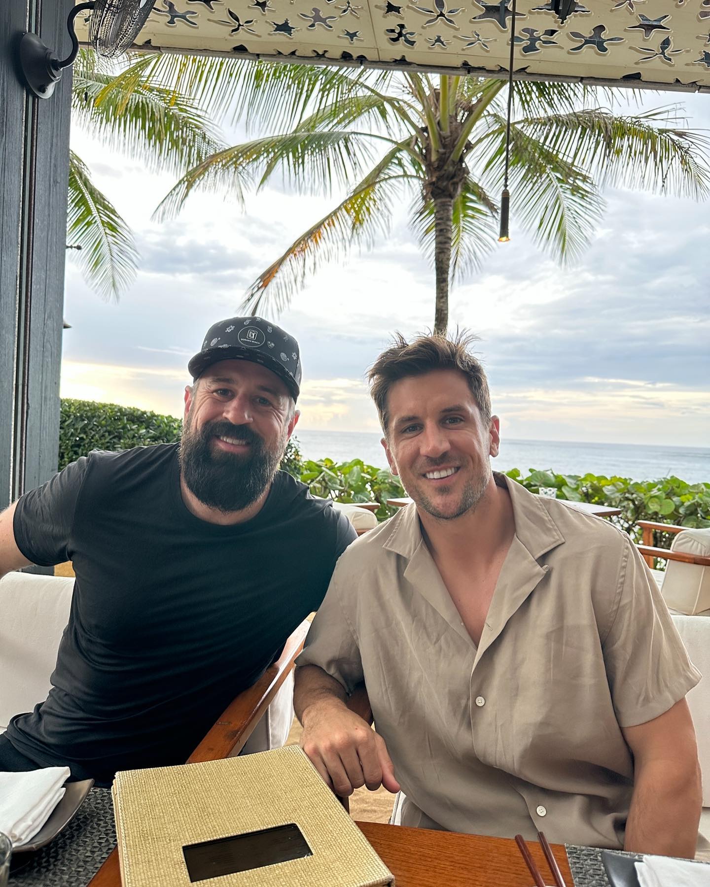 Aaron Rodgers' brothers, Luke and Jordan, smiling at a table outdoors.