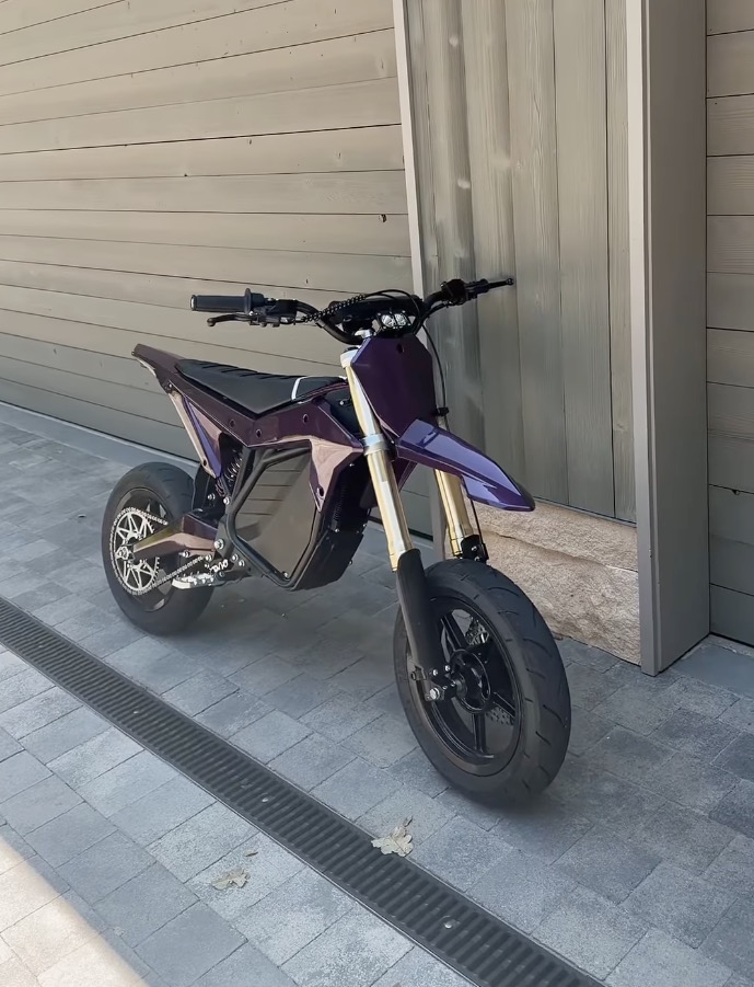 A purple electric dirt bike on a paved driveway.