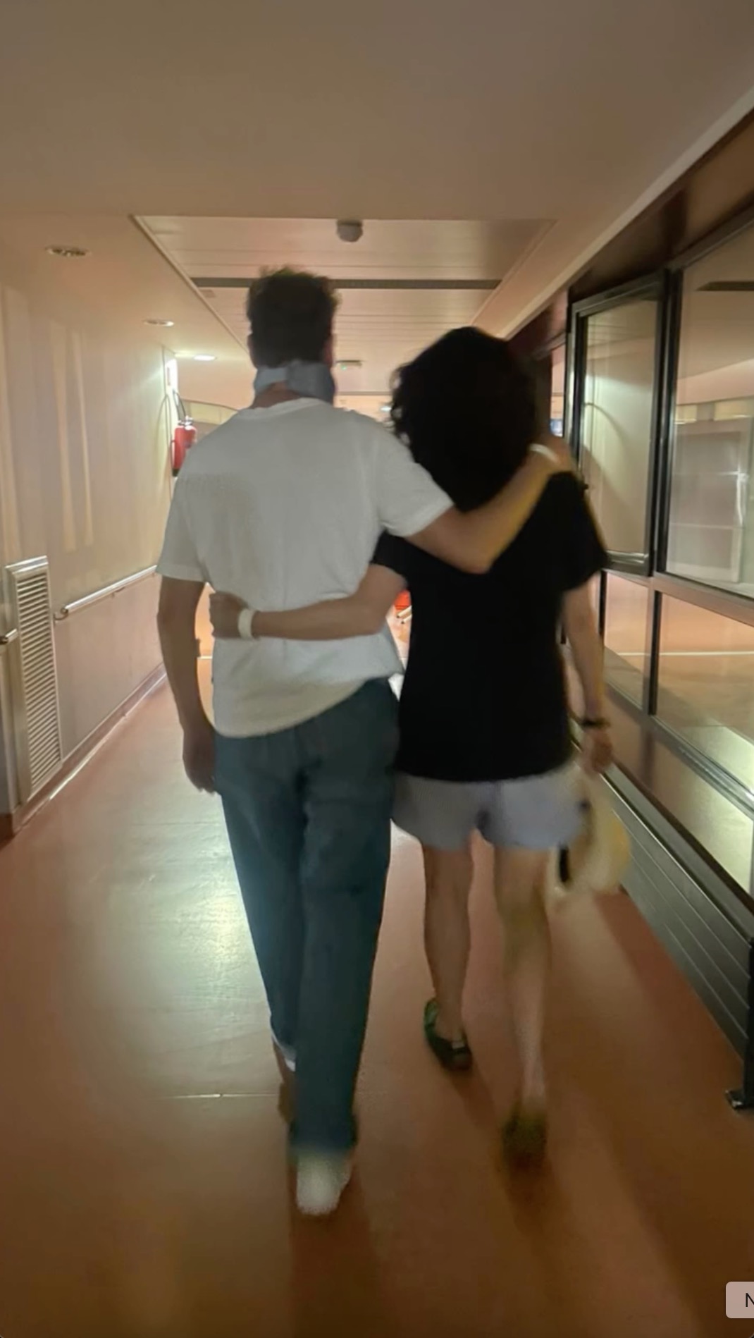 A person in a neck brace being supported by another person as they walk down a hospital hallway after a car crash.