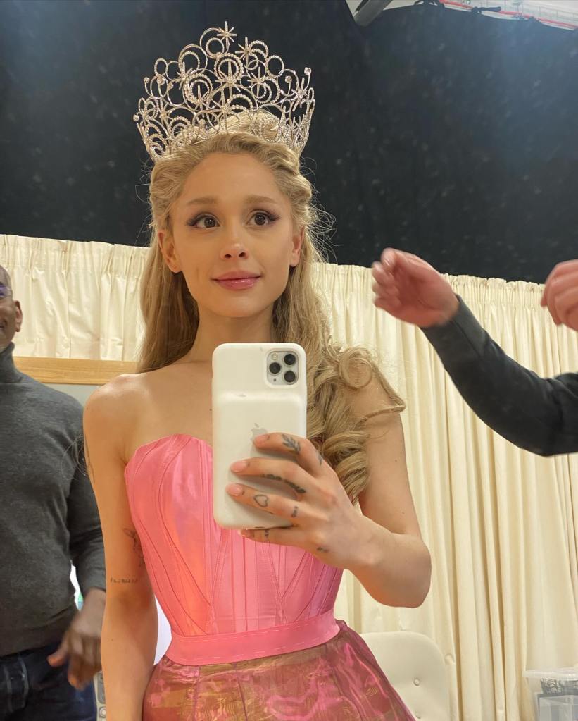 Ariana Grande in a pink dress and tiara taking a mirror selfie.