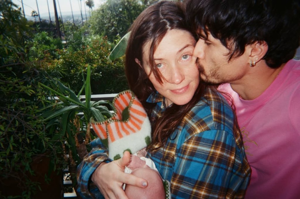 Camille Summers-Valli holding a baby and Charles Melton kissing her cheek.