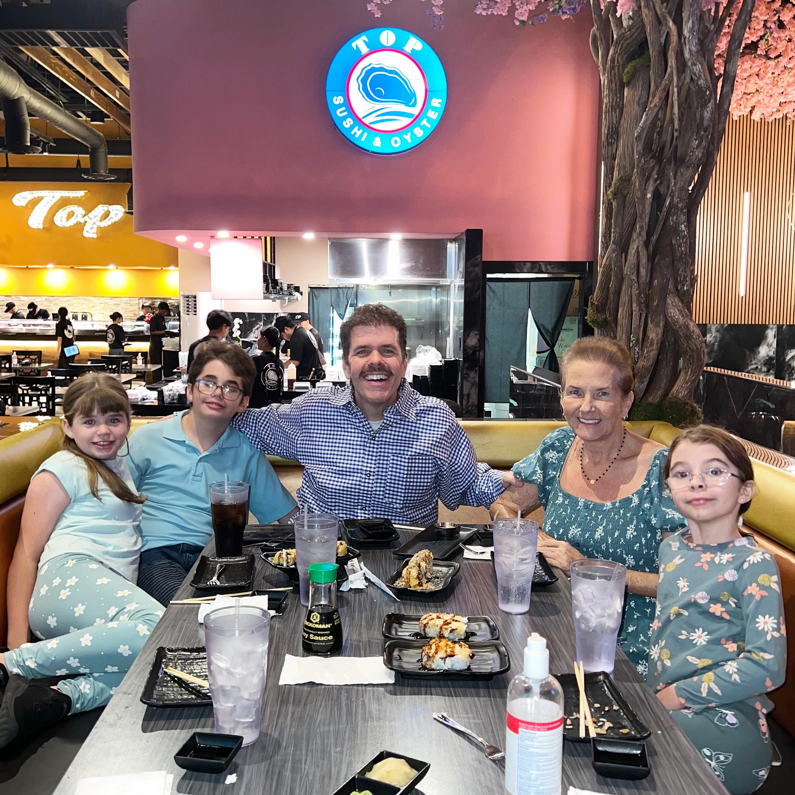 Perez Hilton with his mother and kids enjoying sushi in a restaurant.