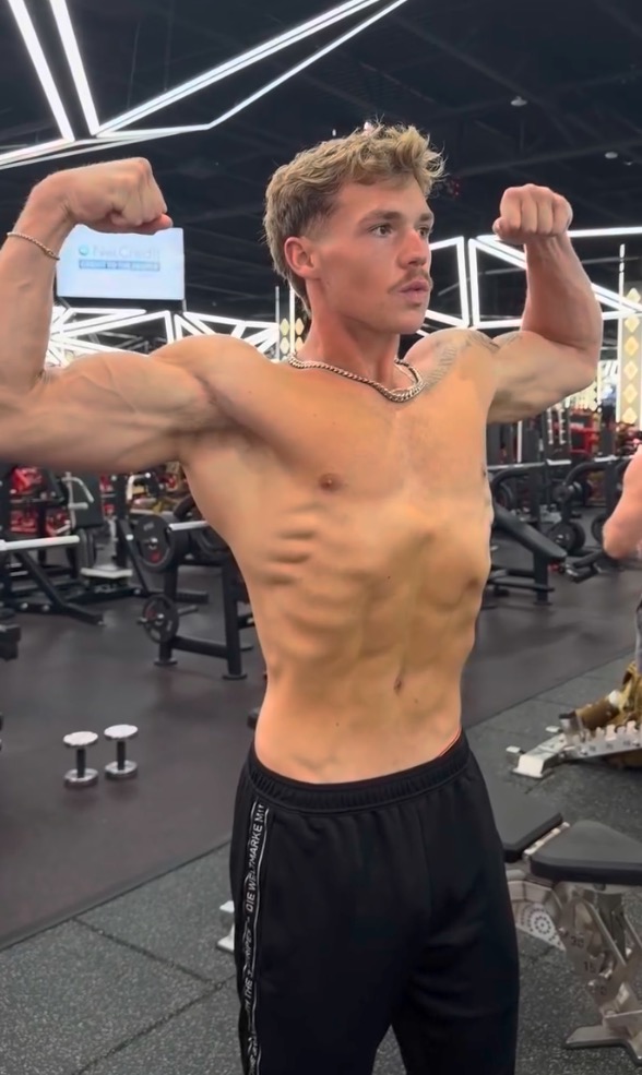 A man flexing his biceps and showing his stomach vacuum in a gym.