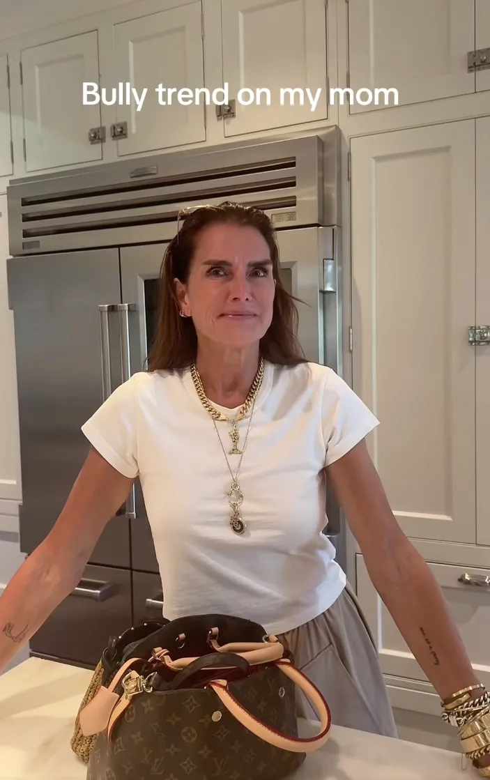 Brooke Shields looking at her daughter, Grier Henchy, with an exasperated expression, next to a Louis Vuitton purse on a kitchen counter.
