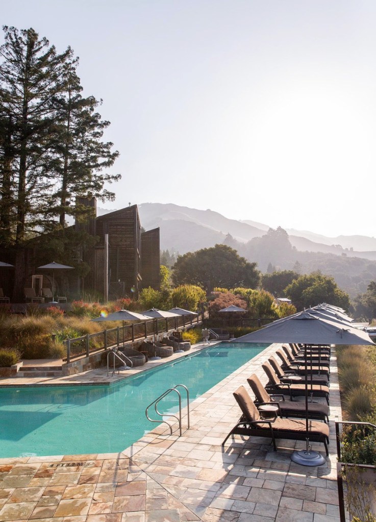 An outdoor swimming pool at Alila Ventana Big Sur, with lounge chairs and umbrellas.