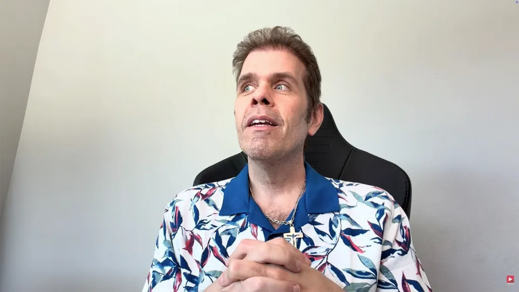 Perez Hilton looking up and to the right, wearing a blue and white patterned shirt and a cross necklace.